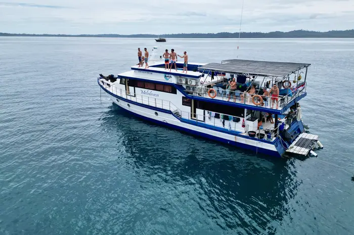 The boat anchored in flat turquoise water with guests aboard